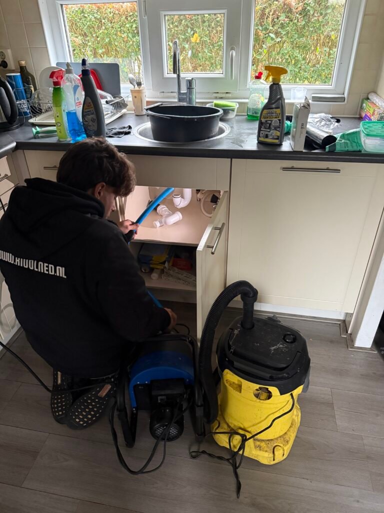 Monteur van Rioolned aan het werk onder een keukenaanrecht