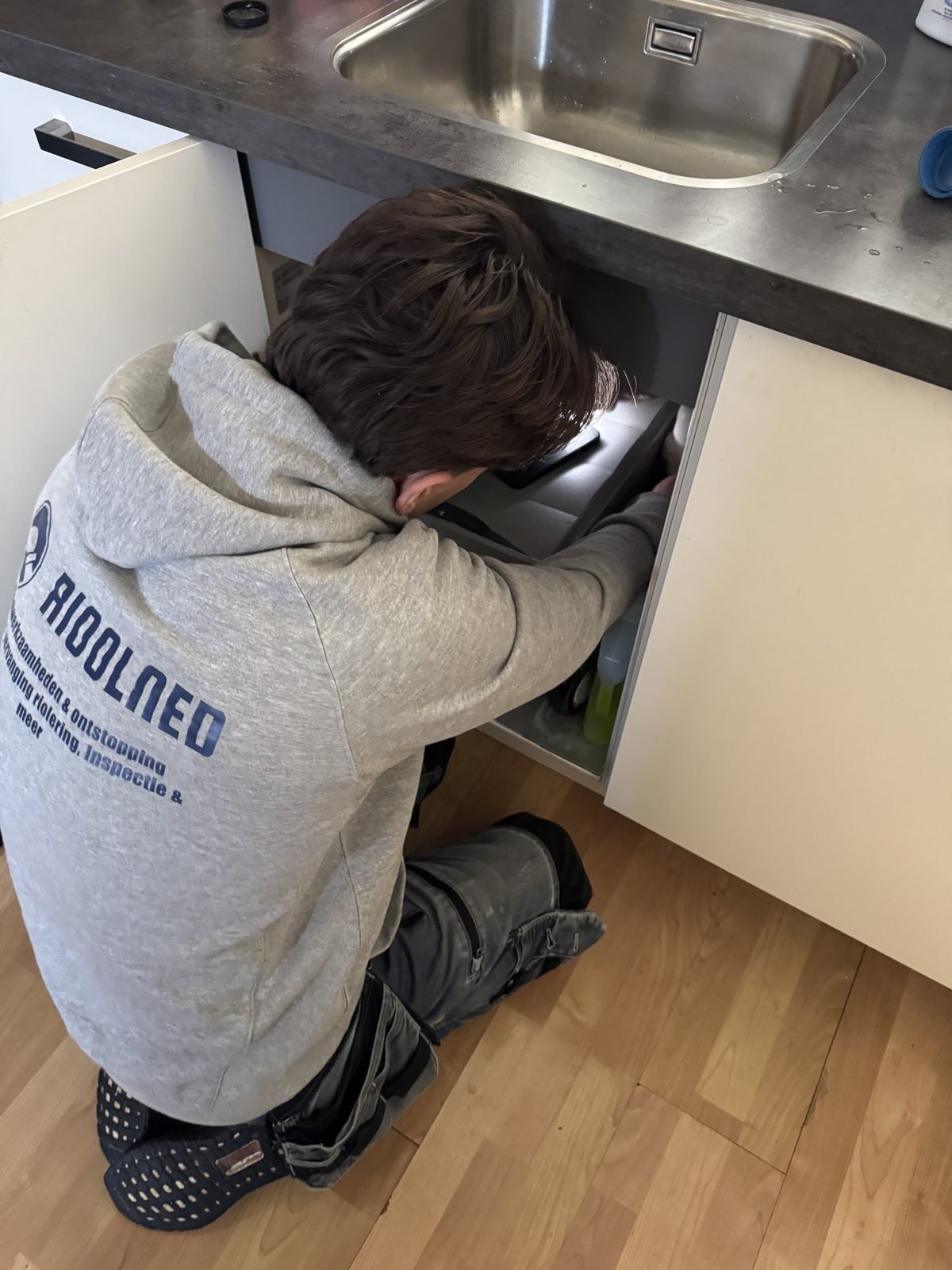 Monteur van Rioolned aan het werk onder een keukenspoelbak