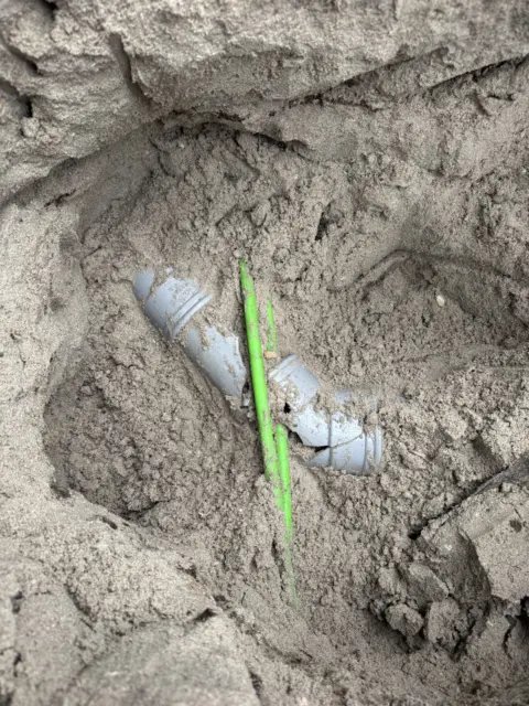 Opengegraven rioolbuis in zandgrond met markering