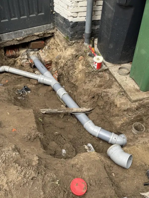 Nieuwe rioolaansluitingen in een sleuf naast een woning